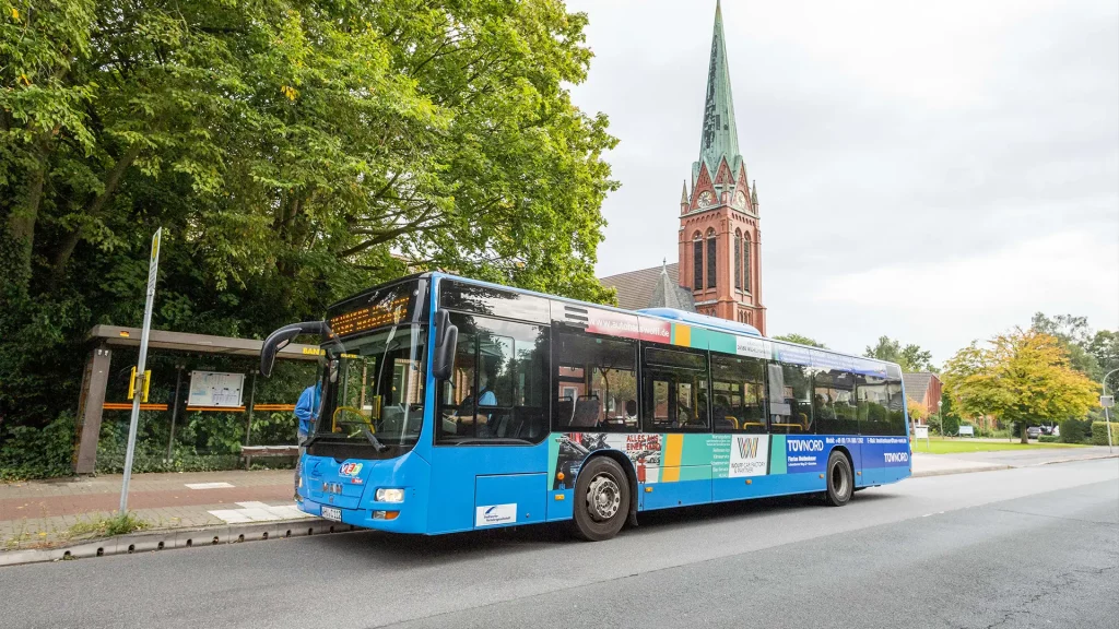 Ein blauer Bus der Stadtwerke Verkehrsgesellschaft Wilhelmshaven hält an der Haltestelle Banter Kirche, um Fahrgäste aufzunehmen.